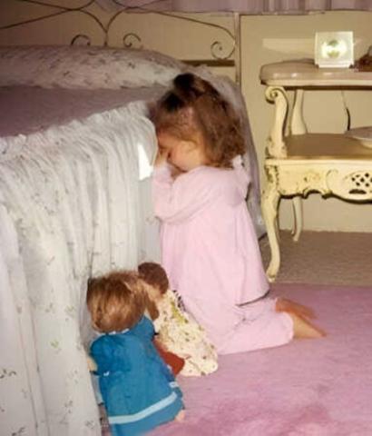 Little girl in prayer by her bedside with her dolls also praying